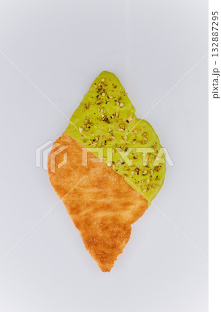 Flaky croissant dipped in green pistachio glaze and crushed nuts on white background 132887295