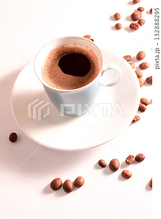 Coffee in a blue cup sits on a white table with coffee beans scattered nearby. Coffee in a blue cup sits on a white table with coffee beans scattered nearby. 132888295
