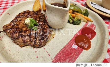 A juicy grilled steak topped with butter and parsley is served with brown sauce, colorful vegetables, and ketchup on a rustic plate, creating a warm and appetizing dining experience full of flavor. A juicy grilled steak topped with butter and parsley is served with brown sauce, colorful vegetables, and ketchup on a rustic plate, creating a warm and appetizing dining experience full of flavor. 132888908
