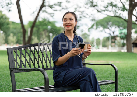 Doctor enjoying coffee break while checking phone in park Doctor enjoying coffee break while checking phone in park 132890757