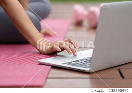 Remote Work and Fitness. Woman using laptop for online workout while seated on exercise mat. 132890945