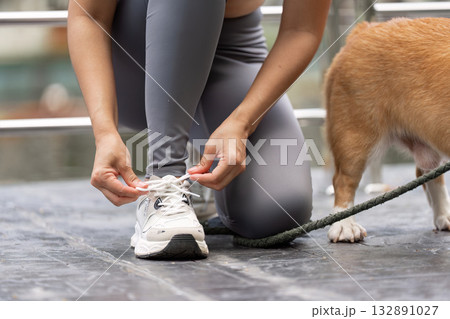 Wellness and Fitness. Woman preparing for a walk with her dog, tying shoelaces outdoors. Wellness and Fitness. Woman preparing for a walk with her dog, tying shoelaces outdoors. 132891027