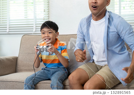 Exciting Gaming Session. A father and son enjoying video games together in a cozy living room. 132891565
