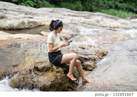 Camping and Nature Connection. Woman relaxing by the river while using her smartphone. Camping and Nature Connection. Woman relaxing by the river while using her smartphone. 132891607