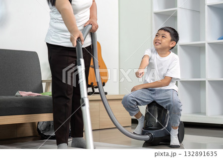 A young boy smiles while assisting an adult with vacuuming, showcasing teamwork and family involvement in household cleaning tasks.. A young boy smiles while assisting an adult with vacuuming, showcasing teamwork and family involvement in household cleaning tasks.. 132891635