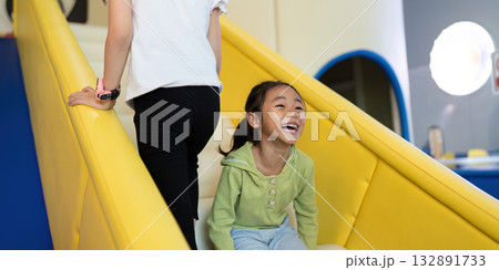 Playful Sliding Fun. Child laughing while climbing up slide, enjoying playful moments in a vibrant environment. 132891733