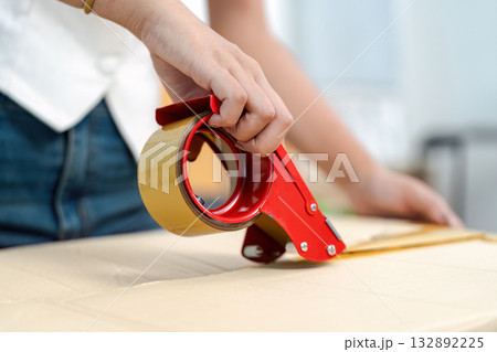 Packing Supplies. Close-up of a hand using a tape dispenser for moving. Packing Supplies. Close-up of a hand using a tape dispenser for moving. 132892225