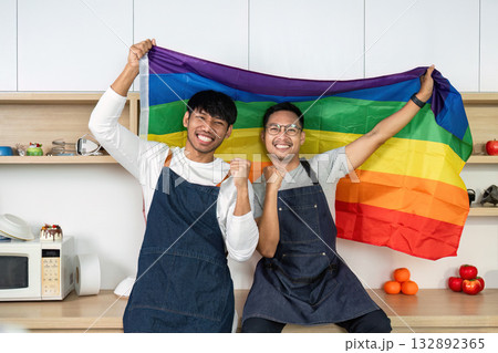 LGBT couple celebrating with pride flag in kitchen. Joyful moment of love and unity. LGBT couple celebrating with pride flag in kitchen. Joyful moment of love and unity. 132892365