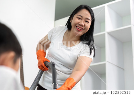 Cleaning and Joy. A woman vacuuming while smiling at her child. 132892513