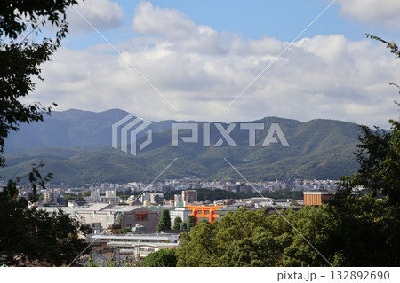 青空と雲と山並みと大きな鳥居のある京都の市街地の街並みの眺めが見える風景 132892690