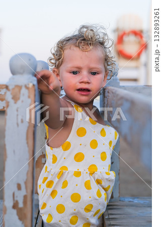 A young girl in a yellow polka dot dress is standing on a wooden fence A young girl in a yellow polka dot dress is standing on a wooden fence 132893261