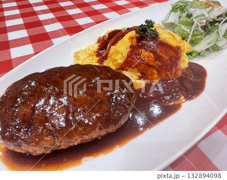 同じお皿に乗る小さめのハンバーグとオムライス 132894098