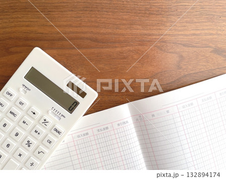 木製テーブルの上の白い電卓と開いた家計簿 132894174