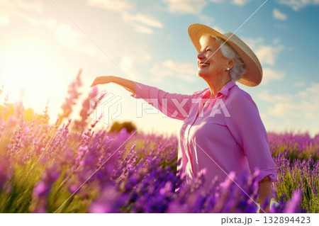 Senior woman enjoying a sunny day in a lavender field with a sunhat and a warm smile 132894423
