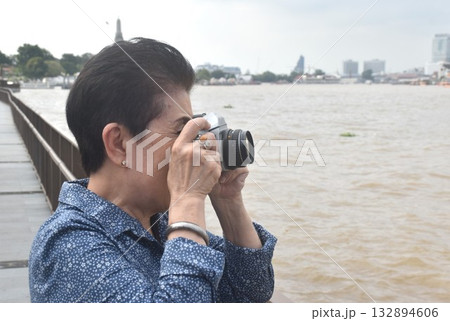 Asian elder woman used film camera shoot landscape of Cho phraya river in Thailand on rainy day 132894606