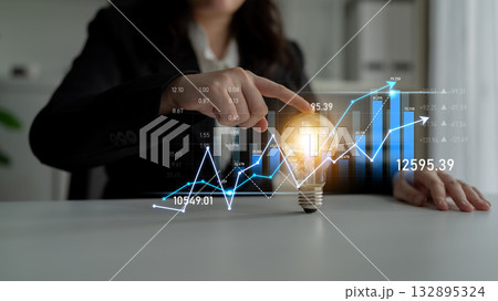 Business professional pointing at light bulb with financial graphs and data analysis in modern office setting representing innovation and growth potential Scalp Business professional pointing at light bulb with financial graphs and data analysis in modern office setting representing innovation and growth potential Scalp 132895324