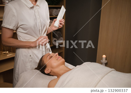Relaxing facial treatment at a spa with a professional applying cream to a woman's face during a soothing wellness session in a serene environment Relaxing facial treatment at a spa with a professional applying cream to a woman's face during a soothing wellness session in a serene environment 132900337
