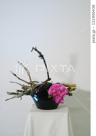 Creative floral arrangement featuring pink flowers and natural branches placed on a neutral background in a simple setting 132900436