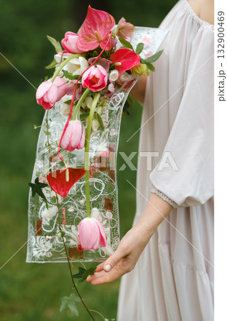 Wedding bouquet with pink tulips and red anthuriums held by a person wearing a light dress in a lush outdoor setting during a sunny day Wedding bouquet with pink tulips and red anthuriums held by a person wearing a light dress in a lush outdoor setting during a sunny day 132900469