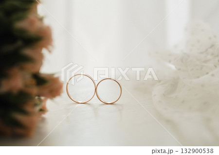 Unique wedding rings placed delicately next to soft flowers and fabric in a bright indoor setting capturing love and connection 132900538