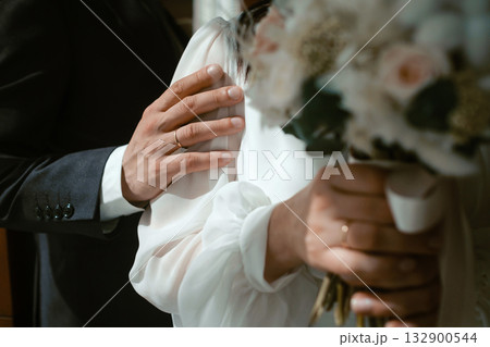 Couple sharing a romantic moment, showcasing wedding rings and bouquet in a soft-lit indoor setting during their wedding ceremony Couple sharing a romantic moment, showcasing wedding rings and bouquet in a soft-lit indoor setting during their wedding ceremony 132900544