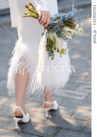 Bride holding a beautiful bouquet of flowers while walking on a cobblestone path near a modern venue during an outdoor wedding ceremony Bride holding a beautiful bouquet of flowers while walking on a cobblestone path near a modern venue during an outdoor wedding ceremony 132900591