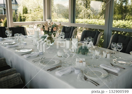 Elegant outdoor dining setup with floral arrangements and glassware on a sunny afternoon 132900599