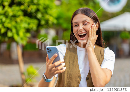 Happy Caucasian young woman using smartphone celebrating win good message news on city town street Happy Caucasian young woman using smartphone celebrating win good message news on city town street 132901878
