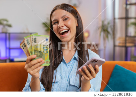 Smiling happy rich young woman counting money euro cash use smartphone, income, saves, lottery win 132901930