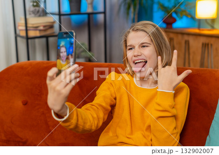 Teenager boy blogger taking selfie with smartphone, making funny facial expressions, posing at home Teenager boy blogger taking selfie with smartphone, making funny facial expressions, posing at home 132902007