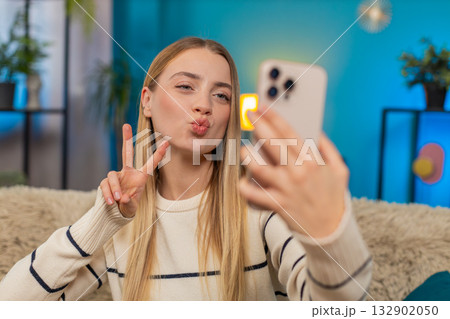 Caucasian woman selfie on sofa smiling making facial expressions holding mobile phone indoors happy Caucasian woman selfie on sofa smiling making facial expressions holding mobile phone indoors happy 132902050
