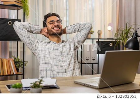 Indian businessman working on laptop putting on earbuds listening music taking a break relaxing 132902053