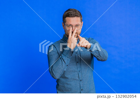 Young man pointing at eyes and camera show I am watching you gesture spying, watching on someone Young man pointing at eyes and camera show I am watching you gesture spying, watching on someone 132902054