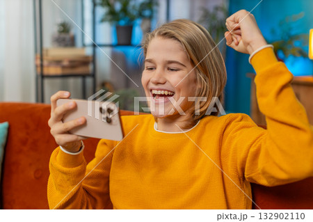 Teenager boy celebrating victory after winning mobile game on smartphone joyful jump on sofa at home Teenager boy celebrating victory after winning mobile game on smartphone joyful jump on sofa at home 132902110