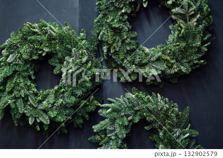 Three handmade evergreen wreaths arranged on a dark surface. Holiday crafting kits, personalized festive decor, seasonal product diversity, consumer co-creation Three handmade evergreen wreaths arranged on a dark surface. Holiday crafting kits, personalized festive decor, seasonal product diversity, consumer co-creation 132902579
