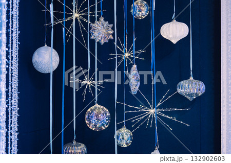 Hanging crystal and glass Christmas ornaments with starburst lights on a dark blue backdrop. Iridescent ornaments, celestial holiday trend, crystal starburst lights, cosmic Christmas 132902603