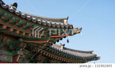 Traditional Korean temple roof architecture with colorful dancheong painted wooden brackets and curved gray tile eaves against clear blue sky Traditional Korean temple roof architecture with colorful dancheong painted wooden brackets and curved gray tile eaves against clear blue sky 132902805