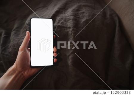 man hand holding phone with white screen over bed on background 132903338