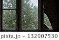 Cracked window with rain in abandoned wooden house during storm with peeling wallpaper and gray light 132907530