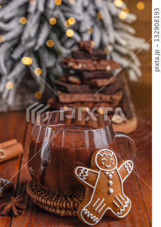 Cup of rich hot chocolate with gingerbread cookie on wooden table in cozy Christmas setting, festive background with bokeh lights, cinnamon sticks and chocolate pieces, winter holiday mood 132908193