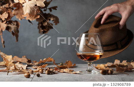Snifter of brandy on a stone table with dried-up oak leaves. Snifter of brandy on a stone table with dried-up oak leaves. 132908789