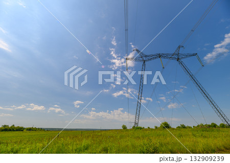 Beautiful Power Lines Stretching Against a Bright Blue Sky and Lush Green Field Land Beautiful Power Lines Stretching Against a Bright Blue Sky and Lush Green Field Land 132909239