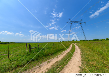 Power Lines Stretching Across a Serene and Vibrant Green Landscape Under a Bright Sky 132909246
