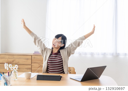 明るい部屋で席に座ったまま背伸びをする若い女性 明るい部屋で席に座ったまま背伸びをする若い女性 132910697