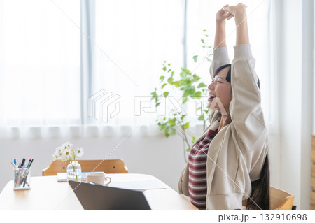 明るい部屋で席に座ったまま背伸びをする若い女性 132910698