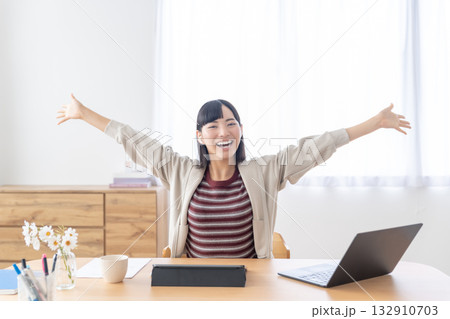 明るい部屋で席に座ったまま背伸びをする若い女性 明るい部屋で席に座ったまま背伸びをする若い女性 132910703