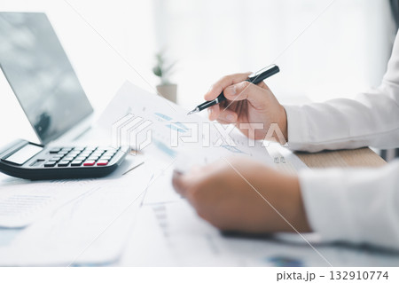 A businesswoman reviews financial report while holding documents and pointing with pen at office desk. Concept of accounting, budget management, financial analysis and corporate business planning. 132910774