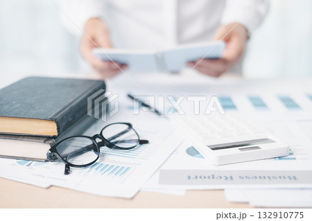 A businesswoman analyzes financial charts and reports with pen while reviewing documents on clipboard at office desk. Concept of accounting, business planning, data analysis and corporate strategy. 132910775