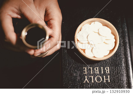 Hands holding communion bread with a wooden bowl and wine cup, symbolizing Holy Communion, the Eucharist, the sacrifice of Jesus Christ and Christian faith in the Lord Supper. 132910930