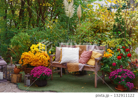 Wooden garden bench with pillows among autumn flowers and colorful foliage in fall backyard Wooden garden bench with pillows among autumn flowers and colorful foliage in fall backyard 132911122